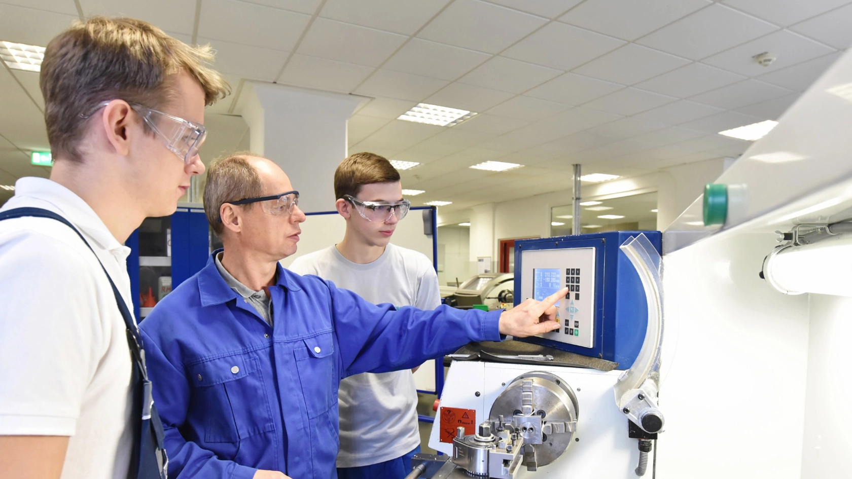 Junge Auszubildende in der technischen Berufsausbildung werden von älteren Trainer auf CNC-Drehmaschinen Maschinen unterrichtet